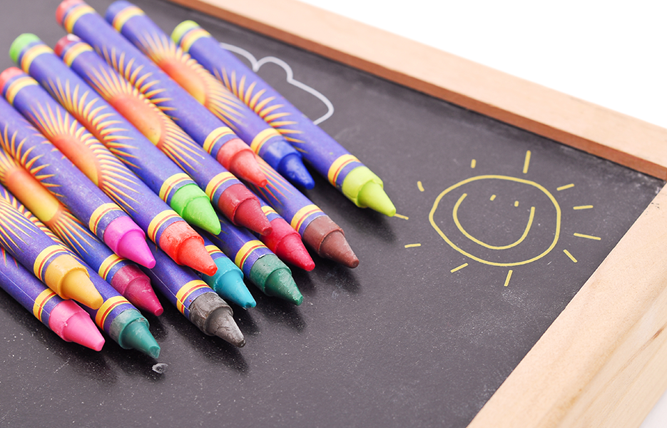 Multiple colored crayons on top of a black chalkboard.